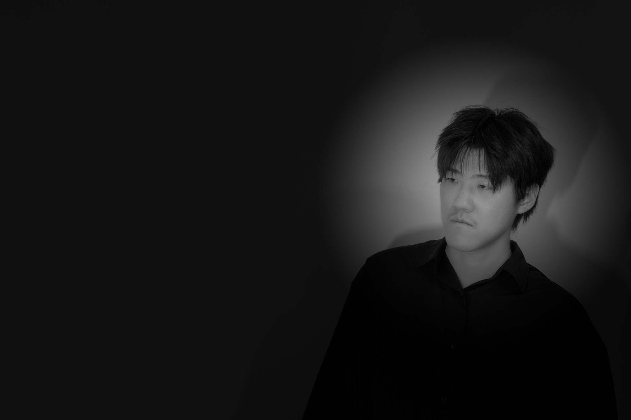 Black-and-white portrait of the photographer Junrui Ye, wearing a dark shirt against a dark background