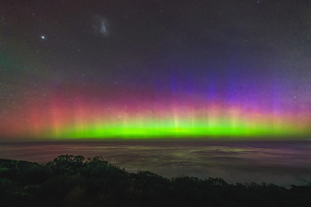 Vivid Southern Lights with bright green base, red middle layer, and purple pillars above the ocean at Muhan Viewpoint.
