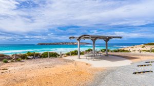 Golden Island Beach car park area in Coffin Bay National Park, featuring a coastal picnic shelter overlooking turquoise ocean waves and rugged cliffs under partly cloudy skies.