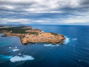 Aerial view of Elliston Clifftop Drive on the Eyre Peninsula, showing rugged coastal cliffs, winding clifftop roads, turquoise shoreline and dramatic storm clouds over the Southern Ocean.