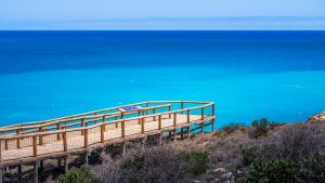 Wooden lookout boardwalk at Head of Bight overlooking calm turquoise and deep-blue waters of the Southern Ocean, with coastal scrubland in the foreground.