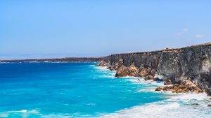 Turquoise and deep-blue ocean waters meeting the towering limestone cliffs at Head of Bight, where waves crash along the rugged coastline of the Great Australian Bight.