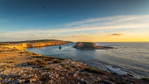 Wedding Cake Island at Lincoln National Park during golden hour, with rugged coastal cliffs, a rocky shoreline foreground and warm sunset light over the ocean.