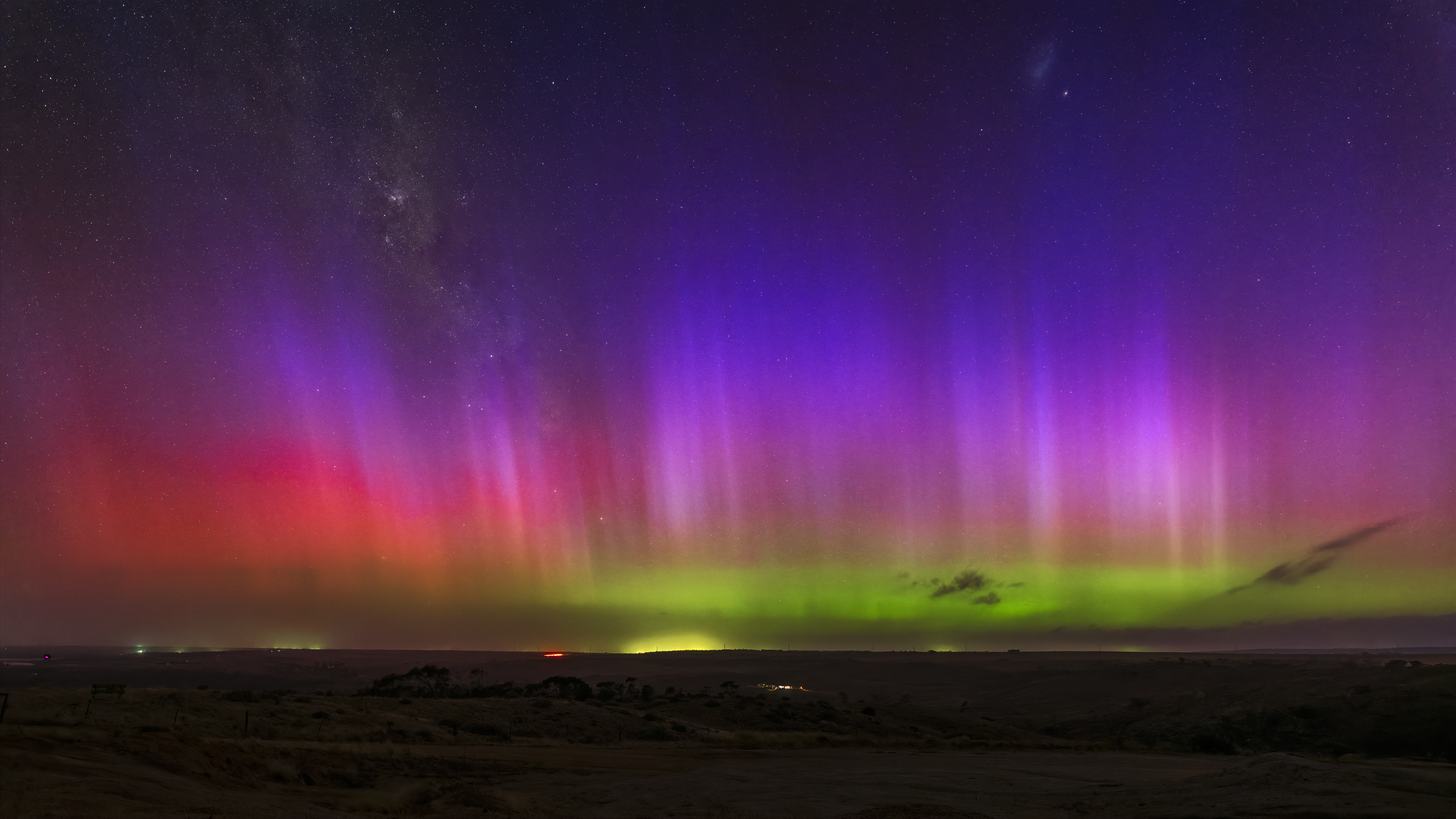 Green and purple aurora australis forming vertical light pillars above the horizon near Mannum, South Australia, beneath a starry night sky.
