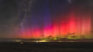 Red and purple auroral rays from Aurora Australis above the rural landscape of Mannum, South Australia, with the Milky Way visible in the night sky.