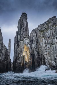 Tall vertical rock pillars along the Tasman Island coast with waves breaking at their base under moody skies.