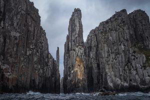 A narrow ocean passage framed by towering sea cliffs at Tasman Island, with dark water and overcast skies.