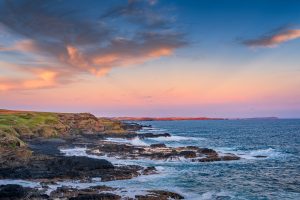 Rocky coastline and ocean waves at The Nobbies during a colourful evening sunset