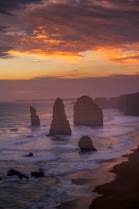 Vertical view of the Twelve Apostles at sunset with glowing orange clouds and ocean waves
